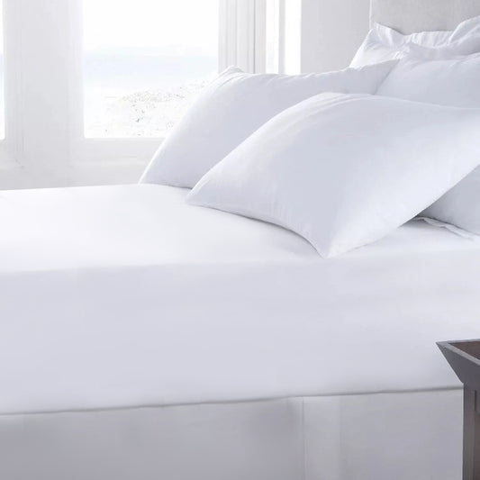 A white deep fitted sheet on a bed, with pillows on top, in a bright room.