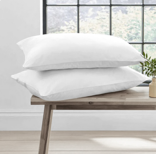 Two white duck feather pillows on a wooden bench with a window in the background.